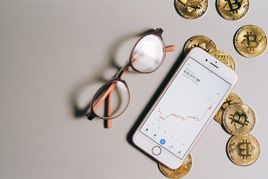 Flat lay of Bitcoin coins, eyeglasses, and smartphone displaying cryptocurrency graph.