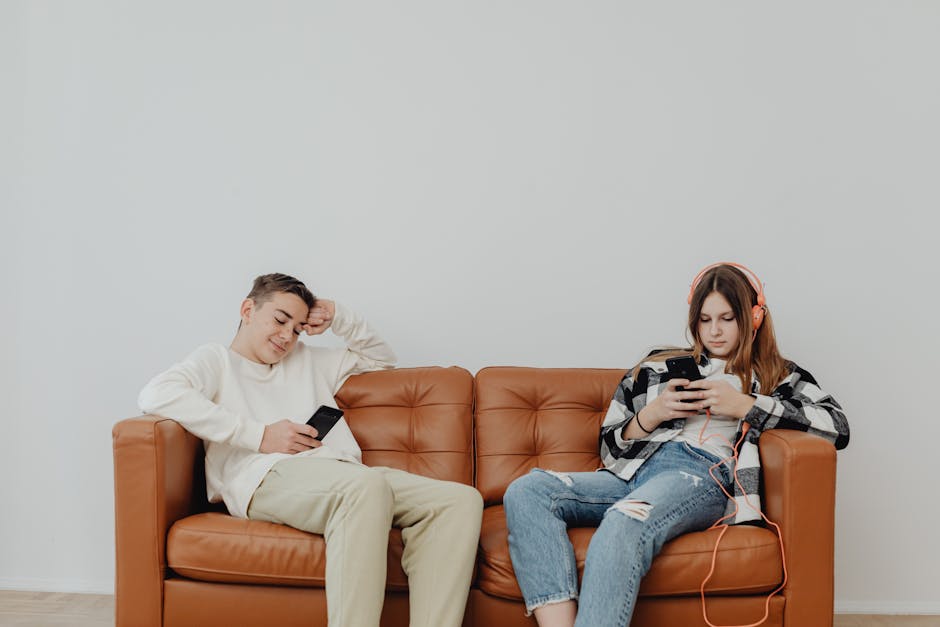 Teenagers lounging on a leather sofa using smartphones, displaying modern leisure.